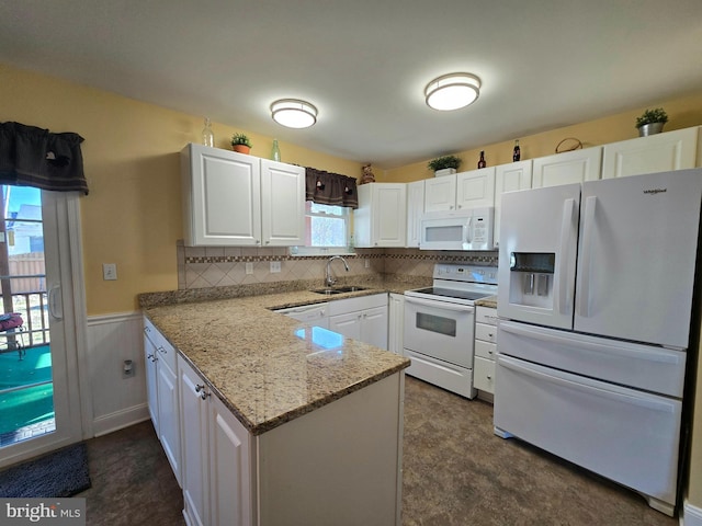 kitchen with white appliances, wainscoting, a sink, and white cabinets