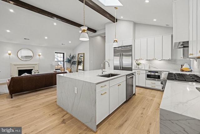 kitchen with stainless steel appliances, sink, decorative light fixtures, white cabinetry, and a center island with sink