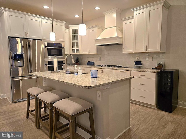 kitchen with an island with sink, beverage cooler, a kitchen breakfast bar, custom exhaust hood, and stainless steel appliances