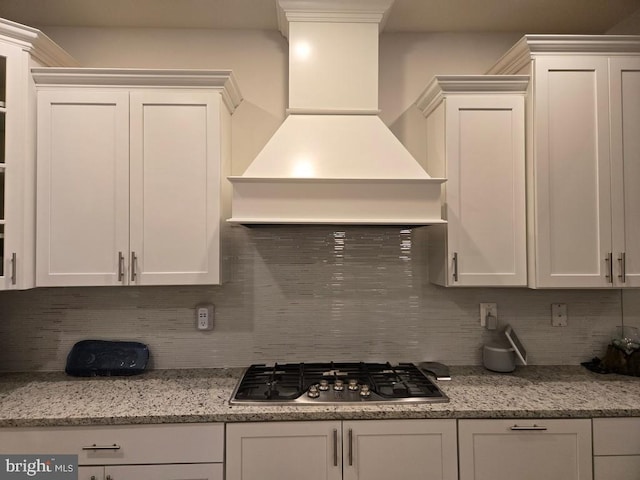 kitchen with premium range hood, white cabinetry, tasteful backsplash, light stone counters, and stainless steel gas stovetop