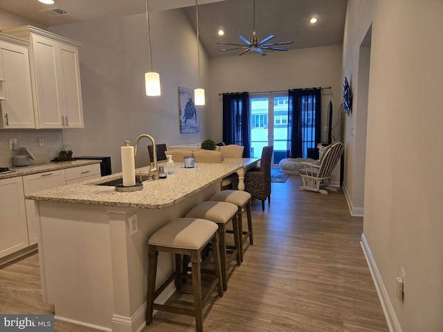 kitchen featuring a breakfast bar, sink, decorative light fixtures, an island with sink, and white cabinets