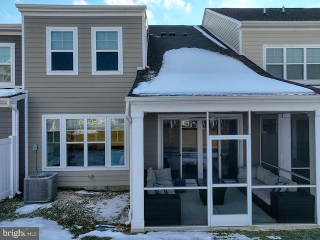 snow covered rear of property with central AC and a sunroom