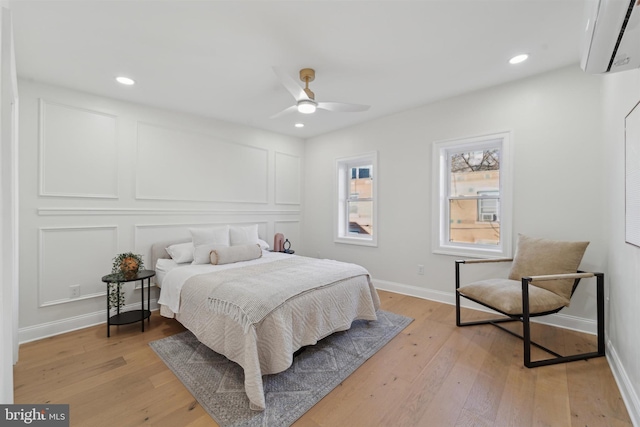 bedroom with light wood-type flooring, a wall unit AC, and ceiling fan