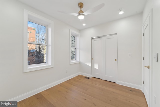 unfurnished bedroom with ceiling fan, light hardwood / wood-style flooring, multiple windows, and a closet