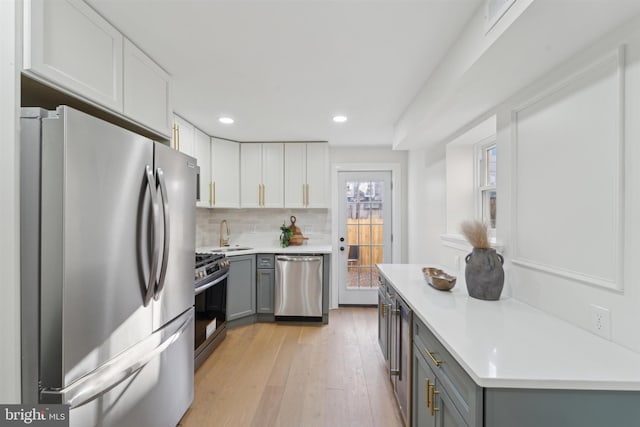 kitchen featuring gray cabinetry, decorative backsplash, light hardwood / wood-style floors, white cabinetry, and stainless steel appliances