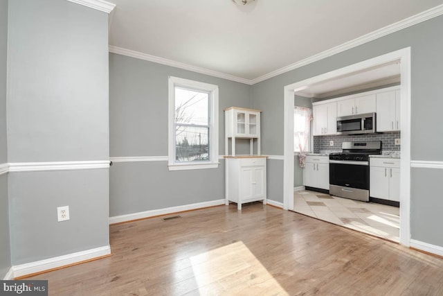 kitchen with tasteful backsplash, white cabinets, stainless steel appliances, crown molding, and light hardwood / wood-style flooring