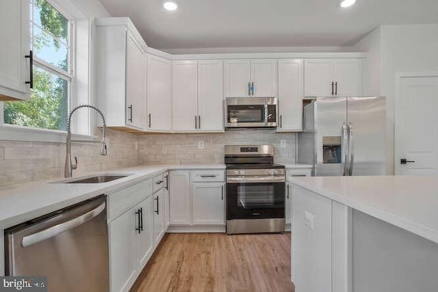 kitchen featuring backsplash, sink, light wood-type flooring, appliances with stainless steel finishes, and white cabinetry