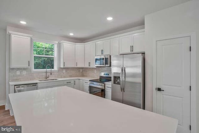 kitchen with appliances with stainless steel finishes, tasteful backsplash, sink, wood-type flooring, and white cabinets