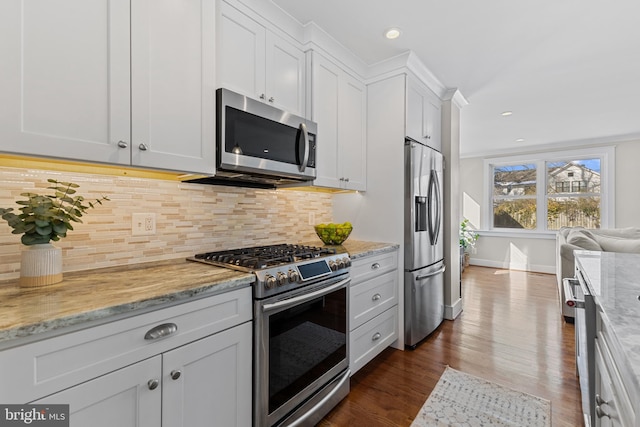 kitchen featuring appliances with stainless steel finishes, white cabinets, tasteful backsplash, light stone countertops, and dark wood-type flooring