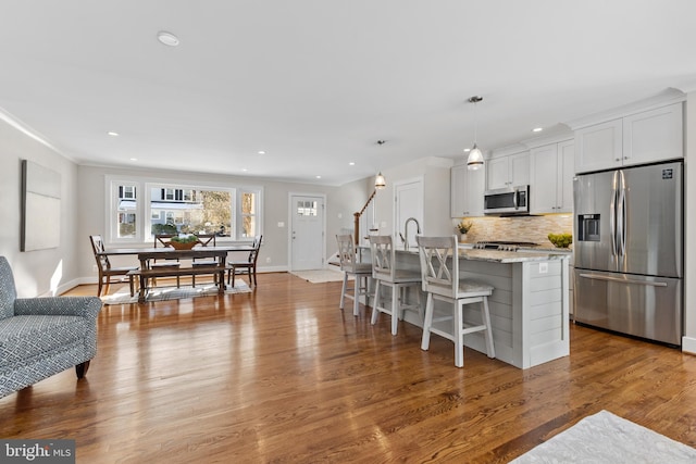 kitchen featuring stainless steel appliances, white cabinets, an island with sink, light stone countertops, and a breakfast bar