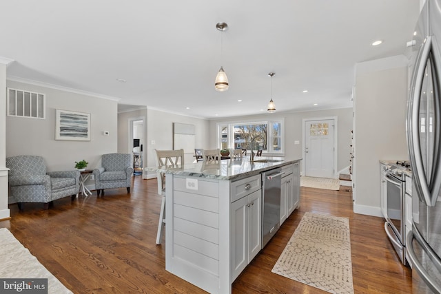 kitchen featuring sink, light stone countertops, a center island with sink, pendant lighting, and appliances with stainless steel finishes