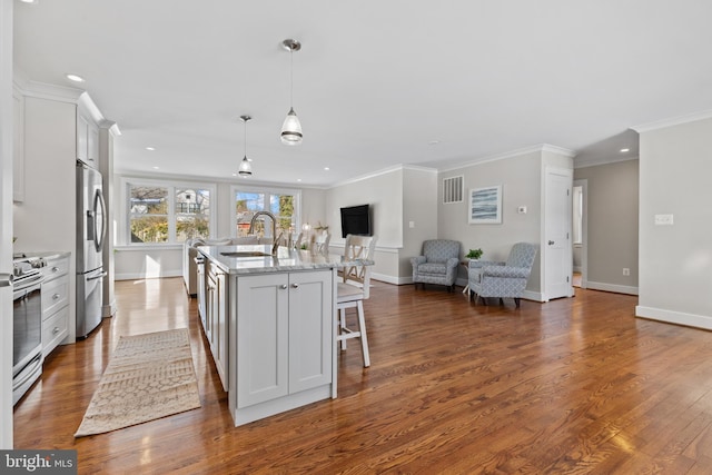 kitchen featuring sink, stainless steel appliances, light stone counters, an island with sink, and pendant lighting