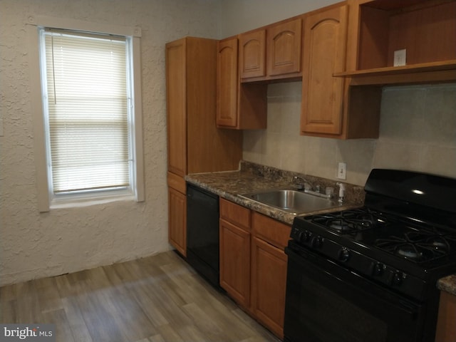 kitchen with black appliances, light hardwood / wood-style flooring, dark stone counters, and sink