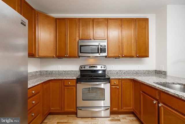 kitchen featuring light stone countertops, appliances with stainless steel finishes, and light hardwood / wood-style flooring