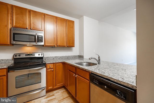 kitchen with light stone countertops, appliances with stainless steel finishes, kitchen peninsula, sink, and light hardwood / wood-style floors