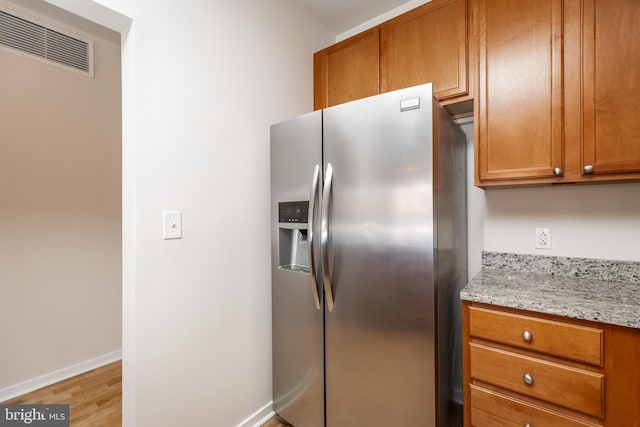 kitchen with stainless steel fridge, light hardwood / wood-style flooring, and light stone counters