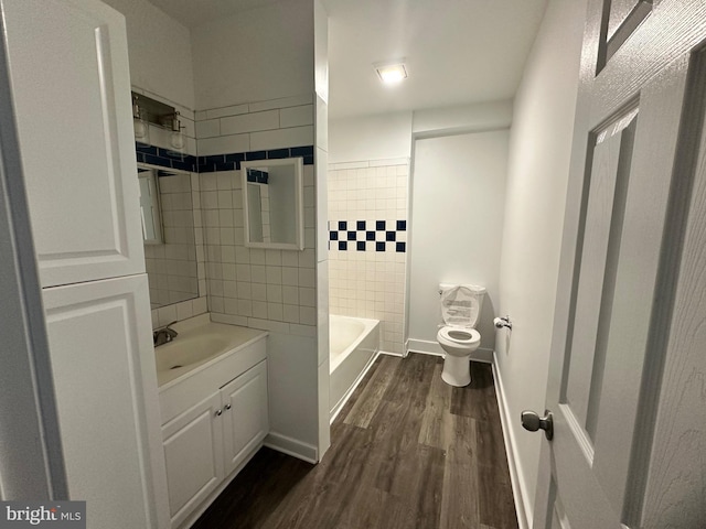 full bathroom with hardwood / wood-style flooring, tiled shower / bath, vanity, and toilet