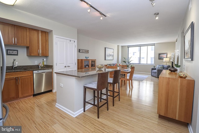 kitchen with dishwasher, light hardwood / wood-style flooring, a center island, a kitchen bar, and dark stone counters