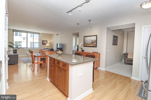 kitchen featuring track lighting, dark stone counters, a kitchen island, and light wood-type flooring