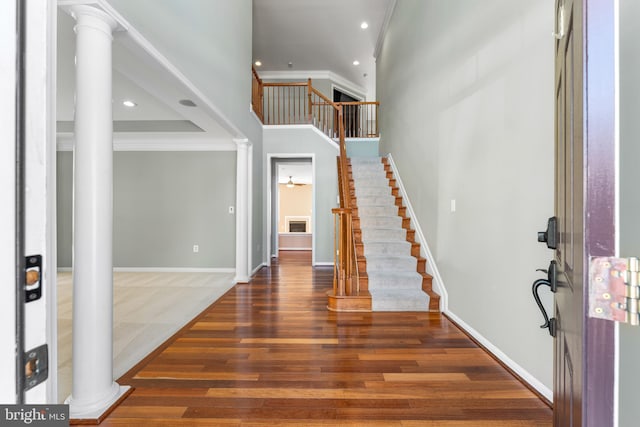 entryway featuring dark wood-type flooring, ceiling fan, ornamental molding, and decorative columns