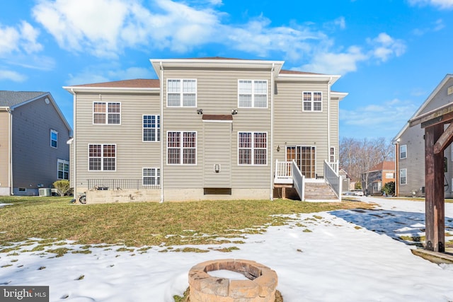 snow covered back of property featuring an outdoor fire pit and a lawn