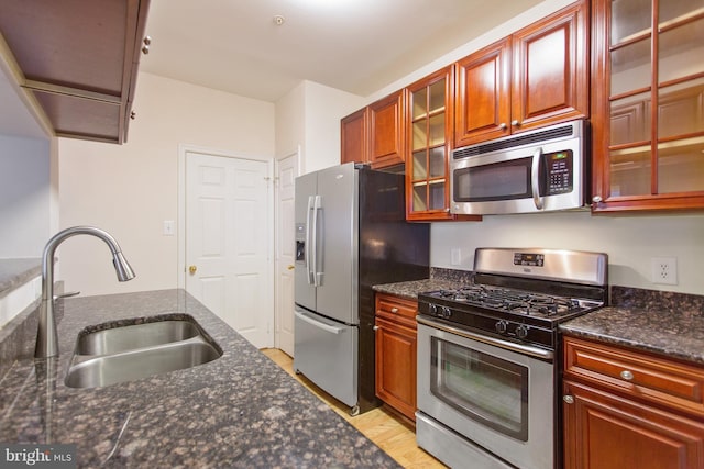 kitchen featuring sink, stainless steel appliances, dark stone counters, and light hardwood / wood-style flooring