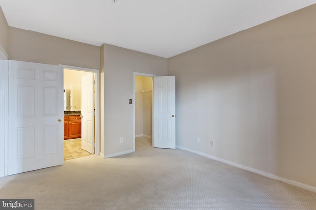 unfurnished bedroom with a walk in closet, light carpet, a closet, and ensuite bath