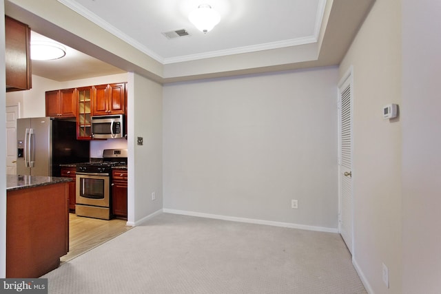 kitchen with ornamental molding, stainless steel appliances, light carpet, and dark stone counters