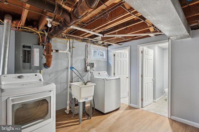 laundry area with electric panel, light wood-type flooring, washing machine and dryer, and sink