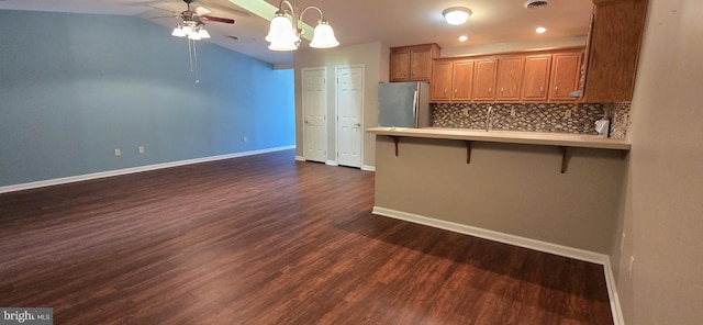 kitchen featuring kitchen peninsula, tasteful backsplash, a kitchen breakfast bar, dark wood-type flooring, and stainless steel refrigerator