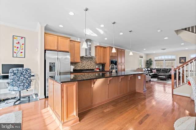 kitchen with stainless steel fridge with ice dispenser, wall chimney range hood, decorative light fixtures, light hardwood / wood-style flooring, and ornamental molding