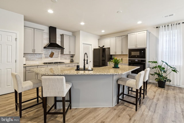 kitchen with a kitchen island with sink, wall chimney range hood, and black appliances