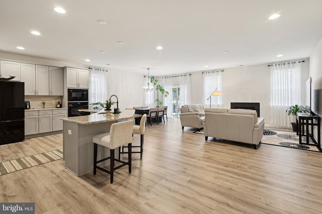 kitchen with hanging light fixtures, light stone countertops, a kitchen island with sink, and black appliances