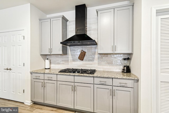 kitchen featuring backsplash, black gas stovetop, light stone countertops, and wall chimney exhaust hood