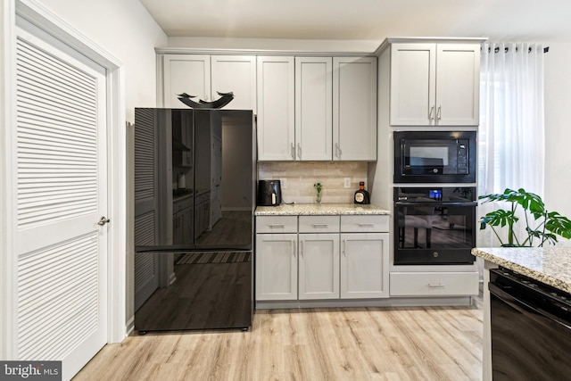 kitchen featuring light stone counters, gray cabinets, light hardwood / wood-style floors, decorative backsplash, and black appliances