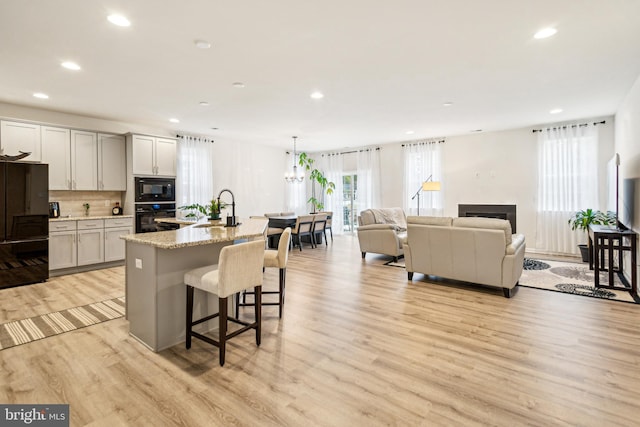 kitchen with hanging light fixtures, an island with sink, light stone counters, and black appliances