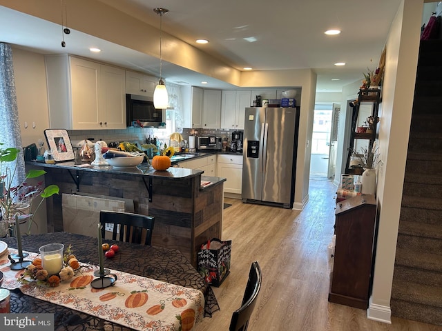 kitchen featuring pendant lighting, stainless steel fridge, tasteful backsplash, white cabinetry, and kitchen peninsula