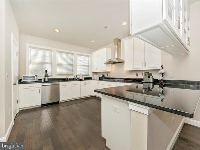 kitchen with dark wood-type flooring, white cabinets, stainless steel dishwasher, wall chimney exhaust hood, and kitchen peninsula