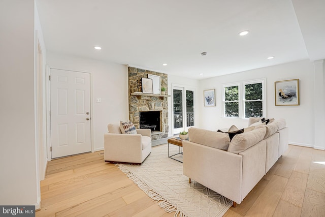 living area with recessed lighting, baseboards, a stone fireplace, and light wood finished floors