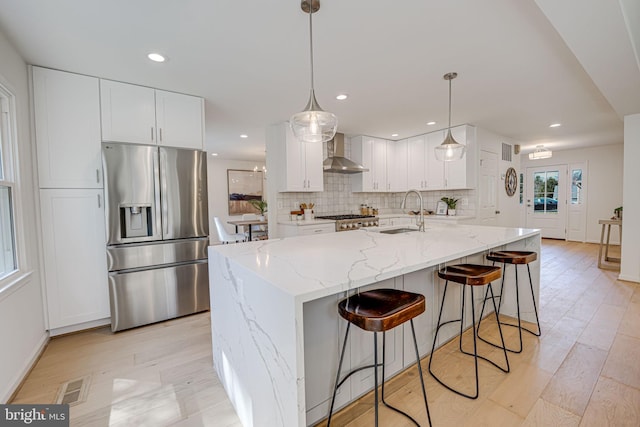 kitchen with tasteful backsplash, visible vents, wall chimney range hood, stainless steel refrigerator with ice dispenser, and a sink