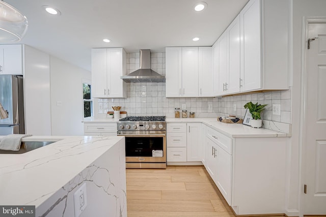 kitchen featuring light wood-style flooring, light stone counters, stainless steel appliances, wall chimney exhaust hood, and white cabinets