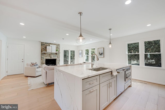 kitchen with a sink, light stone counters, a stone fireplace, light wood finished floors, and hanging light fixtures