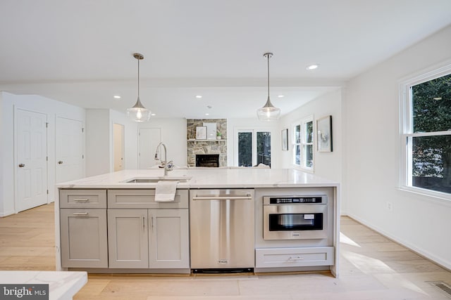 kitchen featuring gray cabinets, a sink, light stone counters, open floor plan, and stainless steel appliances