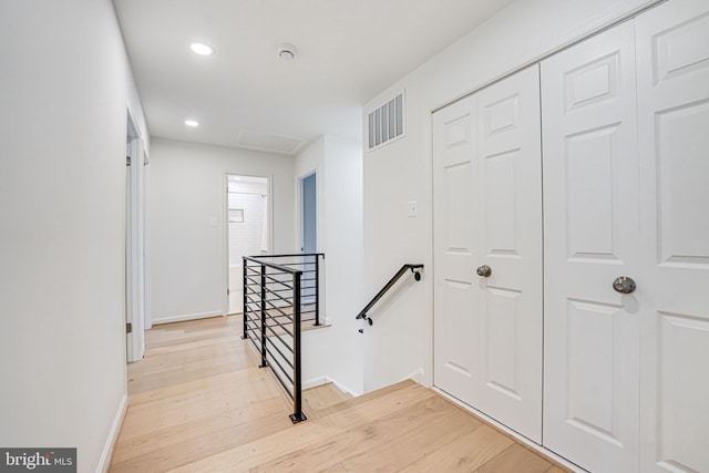 hallway featuring baseboards, visible vents, attic access, an upstairs landing, and light wood-type flooring