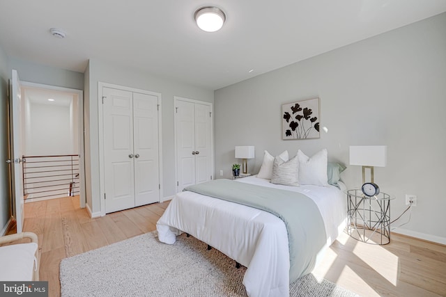 bedroom featuring light wood-style flooring, baseboards, and multiple closets