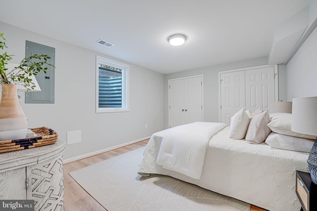 bedroom with wood finished floors, visible vents, baseboards, electric panel, and two closets