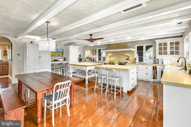 dining room with hardwood / wood-style flooring, ceiling fan, sink, and beamed ceiling