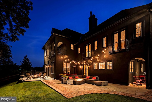 back house at night with a patio, a balcony, and an outdoor living space with a fire pit