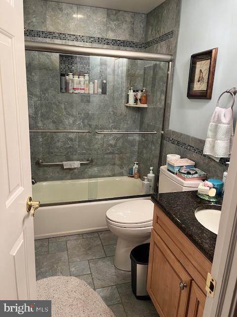 full bathroom featuring vanity, toilet, combined bath / shower with glass door, and tile walls