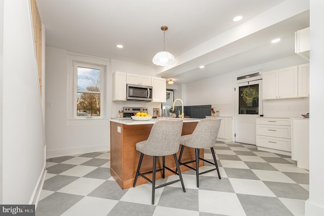 kitchen with a breakfast bar, a kitchen island with sink, white cabinets, hanging light fixtures, and stainless steel appliances